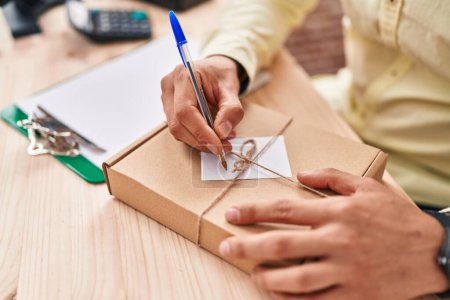 Photo for Young hispanic man ecommerce business worker writing on package at office - Royalty Free Image