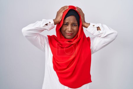 Foto de Mujer árabe joven que usa bufanda islámica tradicional hiyab que sufre de dolor de cabeza desesperada y estresada porque el dolor y la migraña. manos en la cabeza. - Imagen libre de derechos