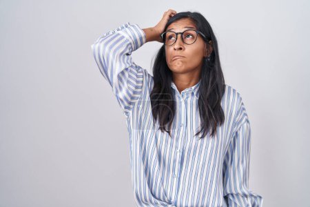 Foto de Young hispanic woman wearing glasses confuse and wondering about question. uncertain with doubt, thinking with hand on head. pensive concept. - Imagen libre de derechos