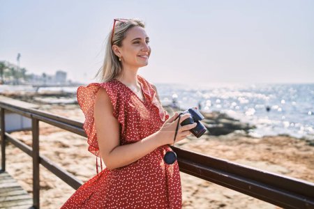 Téléchargez les photos : Jeune fille blonde souriant heureux en utilisant la caméra à la plage - en image libre de droit