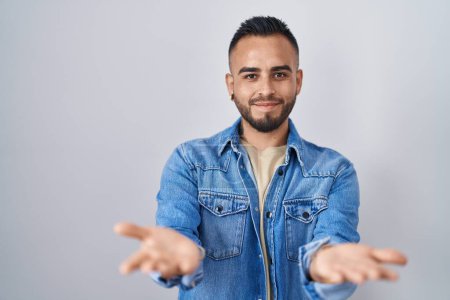 Téléchargez les photos : Young hispanic man standing over isolated background smiling cheerful offering hands giving assistance and acceptance. - en image libre de droit