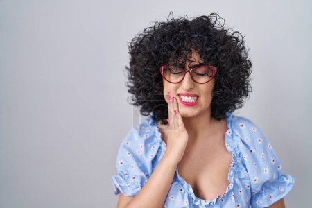 Photo for Young brunette woman with curly hair wearing glasses over isolated background touching mouth with hand with painful expression because of toothache or dental illness on teeth. dentist - Royalty Free Image