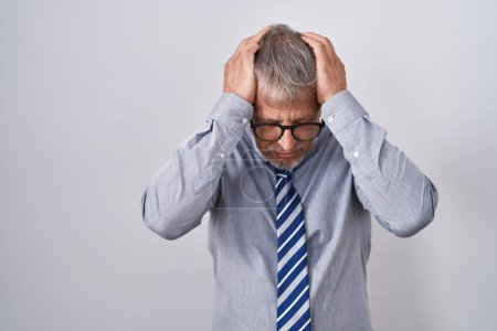 Foto de Hombre de negocios hispano con cabello gris con gafas que sufren de dolor de cabeza desesperado y estresado porque el dolor y la migraña. manos en la cabeza. - Imagen libre de derechos