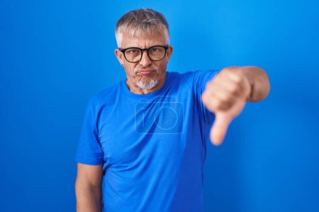 Photo for Hispanic man with grey hair standing over blue background looking unhappy and angry showing rejection and negative with thumbs down gesture. bad expression. - Royalty Free Image