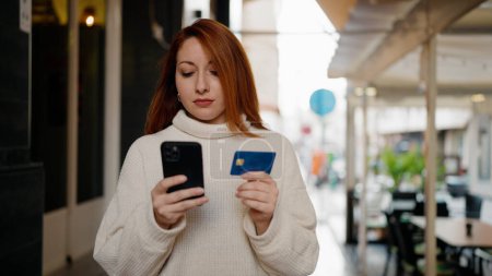 Téléchargez les photos : Jeune rousse femme utilisant smartphone et carte de crédit à la rue - en image libre de droit