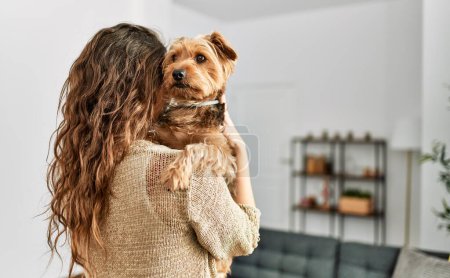 Foto de Joven hermosa mujer hispana abrazando perro de pie en casa - Imagen libre de derechos