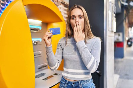 Photo for Young doctor woman holding credit card at cash point covering mouth with hand, shocked and afraid for mistake. surprised expression - Royalty Free Image