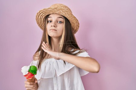 Photo for Teenager girl holding ice cream cutting throat with hand as knife, threaten aggression with furious violence - Royalty Free Image