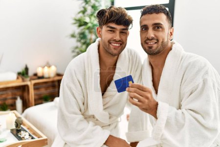 Foto de Two hispanic men couple holding credit card sitting on massage table at beauty center - Imagen libre de derechos