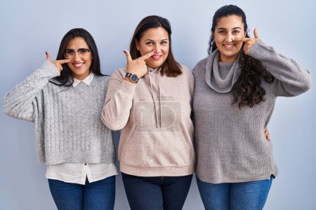 Photo for Mother and two daughters standing over blue background pointing with hand finger to face and nose, smiling cheerful. beauty concept - Royalty Free Image