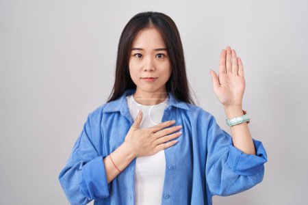 Téléchargez les photos : Young chinese woman standing over white background swearing with hand on chest and open palm, making a loyalty promise oath - en image libre de droit