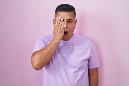 Foto de Joven hombre hispano de pie sobre fondo rosa bostezando cansado cubriendo media cara, ojos y boca con la mano. cara duele en el dolor. - Imagen libre de derechos