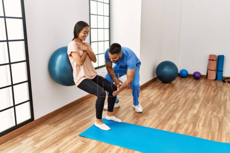 Latein Mann und Frau in Physiotherapeutenuniform bei einer Reha-Sitzung mit Fitnessball im Reha-Zentrum