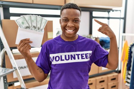 Téléchargez les photos : Jeune homme bénévole africain tenant des billets en dollars pointant du doigt un sourire heureux et fier - en image libre de droit