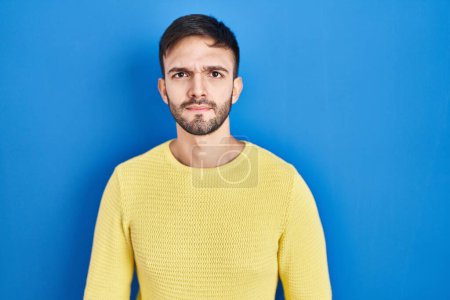 Photo for Hispanic man standing over blue background skeptic and nervous, frowning upset because of problem. negative person. - Royalty Free Image