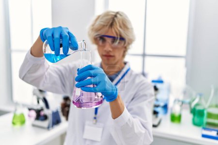Foto de Joven hombre rubio científico vertiendo líquido en tubo de ensayo en el laboratorio - Imagen libre de derechos