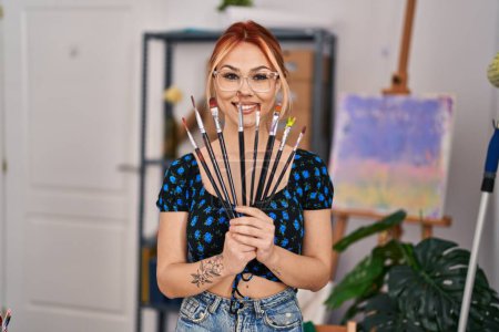 Photo for Young caucasian woman artist smiling confident holding paintbrushes at art studio - Royalty Free Image