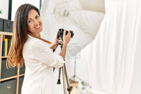 Foto de Middle age hispanic woman photographer smiling confident using camera at photography studio - Imagen libre de derechos