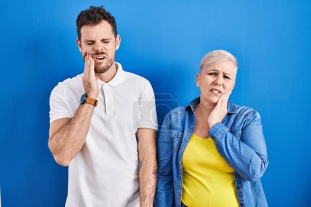Photo for Young brazilian mother and son standing over blue background touching mouth with hand with painful expression because of toothache or dental illness on teeth. dentist - Royalty Free Image