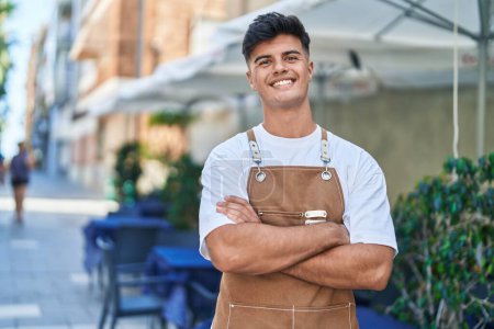 Photo for Young hispanic man waiter smiling confident standing with arms crossed gesture at coffee shop terrace - Royalty Free Image