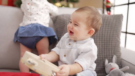 Foto de Adorable niño sosteniendo pandereta sentado en el sofá por el árbol de Navidad en casa - Imagen libre de derechos