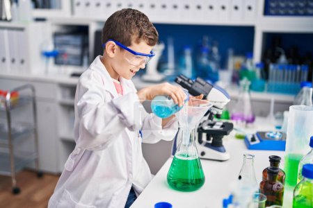 Téléchargez les photos : Enfant blond portant un uniforme scientifique mesurant le liquide au laboratoire - en image libre de droit