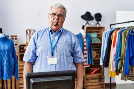 Photo for Senior man with grey hair working as manager at retail boutique sticking tongue out happy with funny expression. emotion concept. - Royalty Free Image