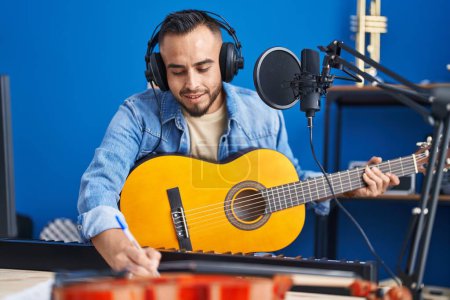 Photo for Young hispanic man artist composing song playing classical guitar at music studio - Royalty Free Image