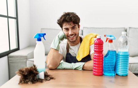 Photo for Young hispanic man smiling confident leaning on table with cleaning products at home - Royalty Free Image