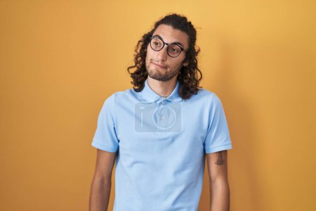 Photo for Young hispanic man standing over yellow background smiling looking to the side and staring away thinking. - Royalty Free Image