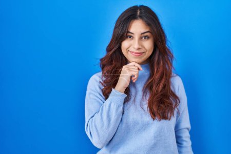 Photo for Hispanic young woman standing over blue background with hand on chin thinking about question, pensive expression. smiling and thoughtful face. doubt concept. - Royalty Free Image