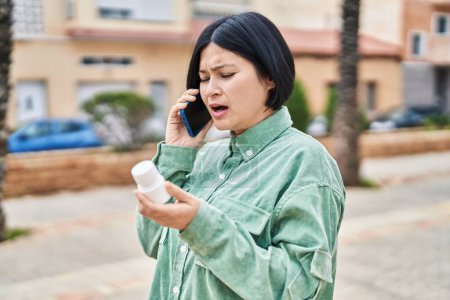 Téléchargez les photos : Jeune femme chinoise parlant sur le smartphone tenant des pilules à la rue - en image libre de droit