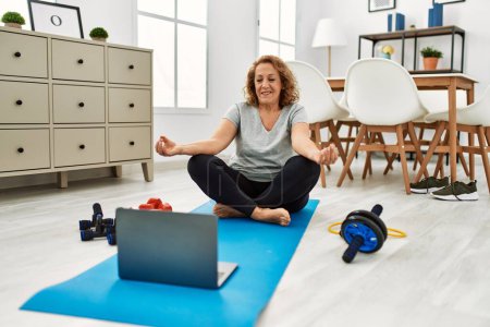 Foto de Mujer caucásica de mediana edad utilizando el yoga de entrenamiento portátil en casa - Imagen libre de derechos