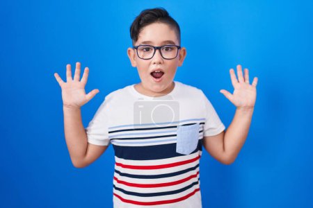 Photo for Young hispanic kid standing over blue background celebrating crazy and amazed for success with arms raised and open eyes screaming excited. winner concept - Royalty Free Image