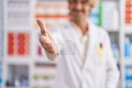 Foto de Joven farmacéutico sonriendo con confianza estrechan la mano en la farmacia - Imagen libre de derechos