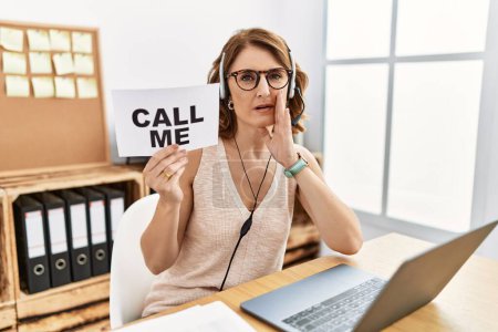 Photo for Middle age brunette woman wearing operator headset holding call me banner hand on mouth telling secret rumor, whispering malicious talk conversation - Royalty Free Image