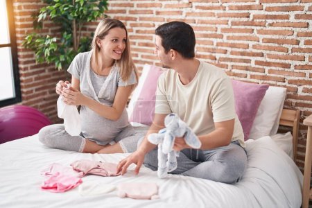 Téléchargez les photos : Homme et femme couple tenant des vêtements et poupée au bébé dans la chambre - en image libre de droit