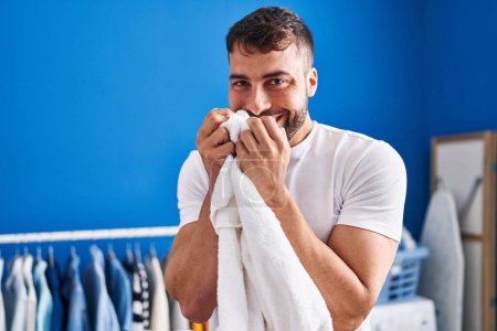 Photo for Young hispanic man smelling towel hanging clothes on clothesline at laundry room - Royalty Free Image