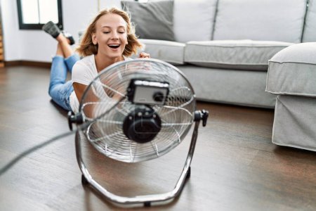 Foto de Young blonde woman smiling confident using fan at home - Imagen libre de derechos