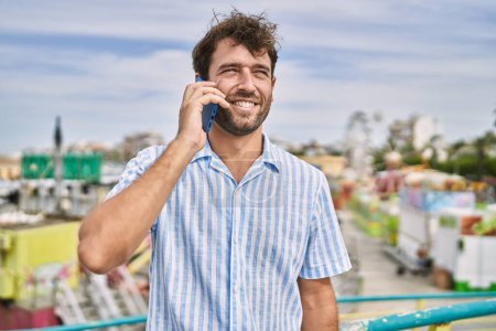 Téléchargez les photos : Jeune homme hispanique souriant heureux de parler sur le smartphone au parc d'attractions. - en image libre de droit