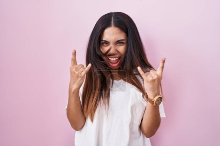 Téléchargez les photos : Jeune femme arabe debout sur fond rose criant avec une expression folle faire symbole rock avec les mains en l'air. star de la musique. concept de musique lourde. - en image libre de droit
