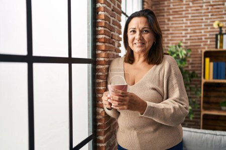 Téléchargez les photos : Middle age hispanic woman drinking coffee standing at home - en image libre de droit
