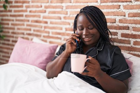 Foto de Mujer afroamericana hablando en smartphone bebiendo café en el dormitorio - Imagen libre de derechos