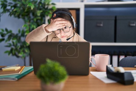 Photo for Woman with down syndrome working at the office wearing headset stressed and frustrated with hand on head, surprised and angry face - Royalty Free Image