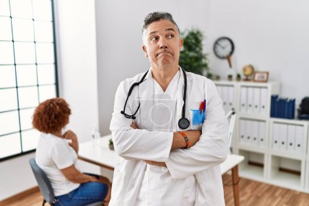 Photo for Middle age doctor man at the clinic with a patient smiling looking to the side and staring away thinking. - Royalty Free Image