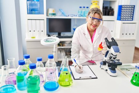 Foto de Young hispanic woman wearing scientist uniform analysing urine test tube at laboratory - Imagen libre de derechos