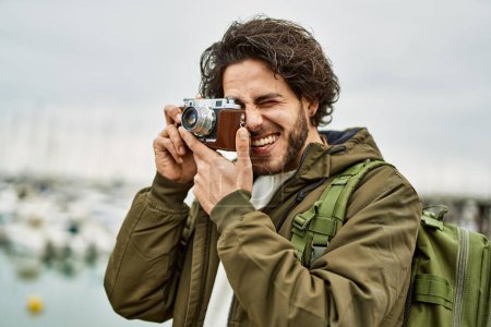 Téléchargez les photos : Bel homme hispanique en utilisant la caméra vintage par port de marina - en image libre de droit