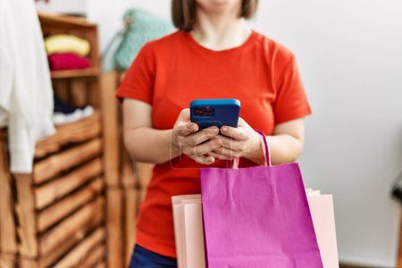 Téléchargez les photos : Femme brune avec syndrome du duvet tenant des sacs à provisions à l'aide d'un smartphone au magasin de détail - en image libre de droit