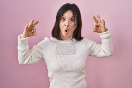 Téléchargez les photos : Femme avec le syndrome du duvet debout sur fond rose regardant surpris et choqué faisant ok symbole d'approbation avec les doigts. expression folle - en image libre de droit