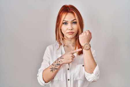 Photo for Young caucasian woman standing over isolated background in hurry pointing to watch time, impatience, looking at the camera with relaxed expression - Royalty Free Image